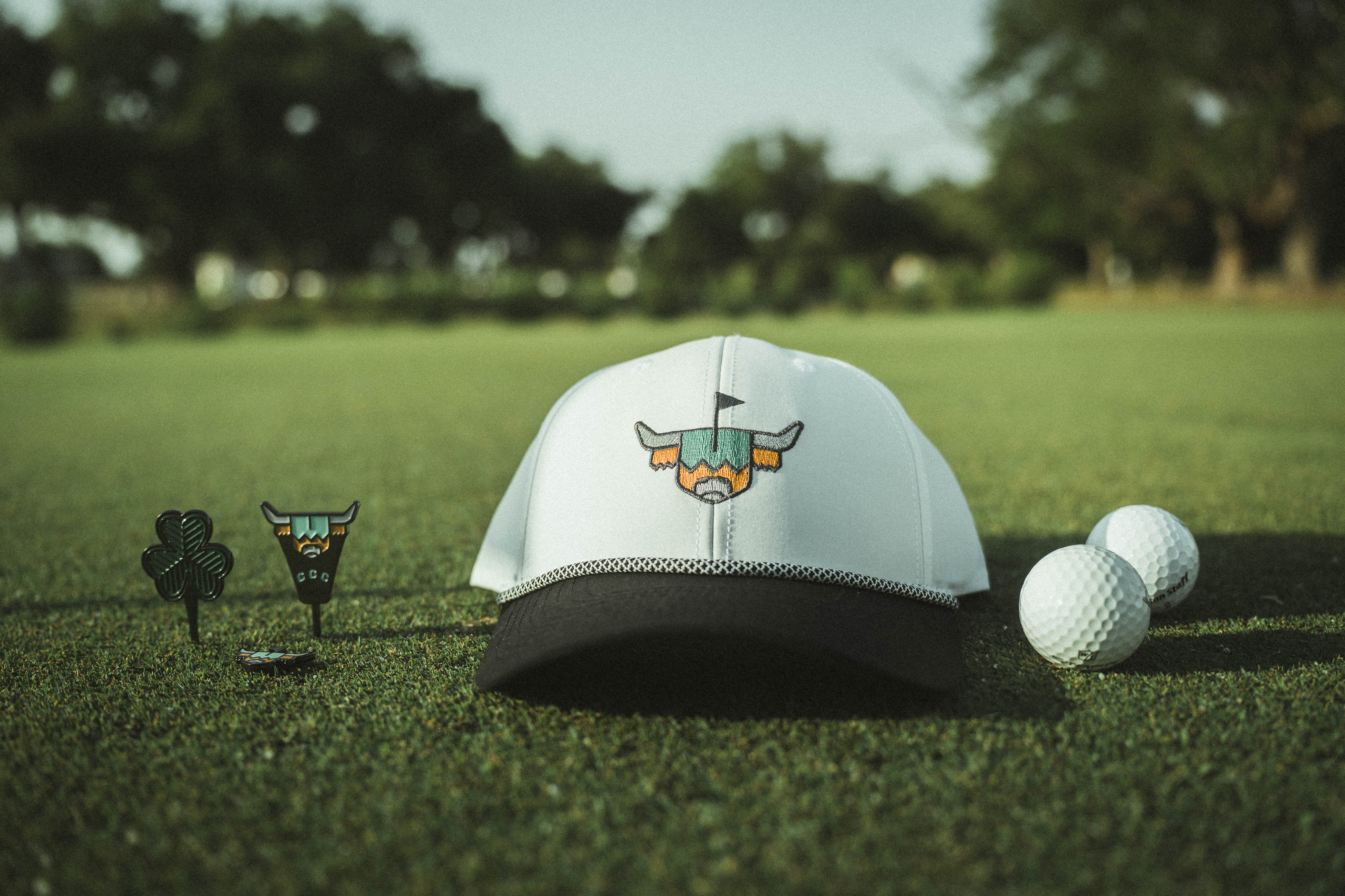 Caddy Collective Culture golf accessories on the green, featuring a hat, divot tool, and golf ball under soft morning light.