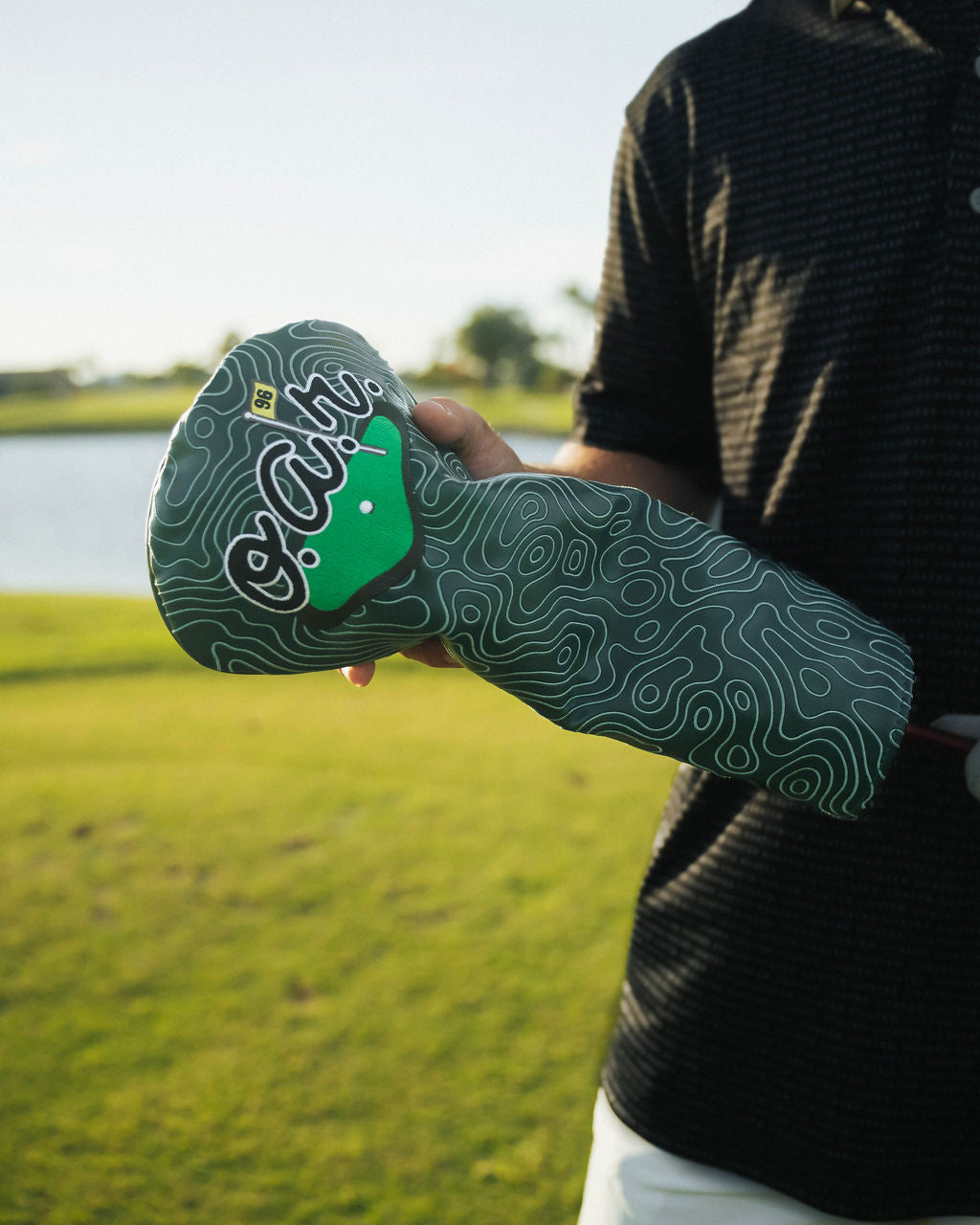Person holding a golf club head cover with a scenic background