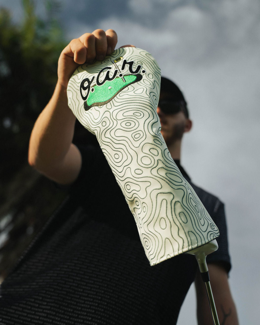 Person holding a golf club head cover with a design and text on a blurred background