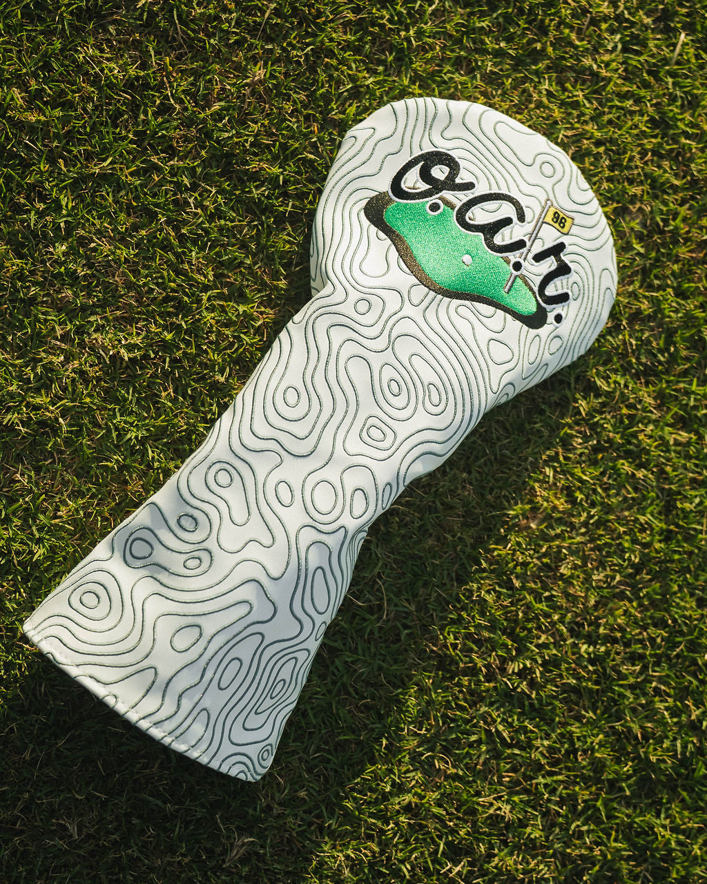 Golf club head cover with a brand logo on grass