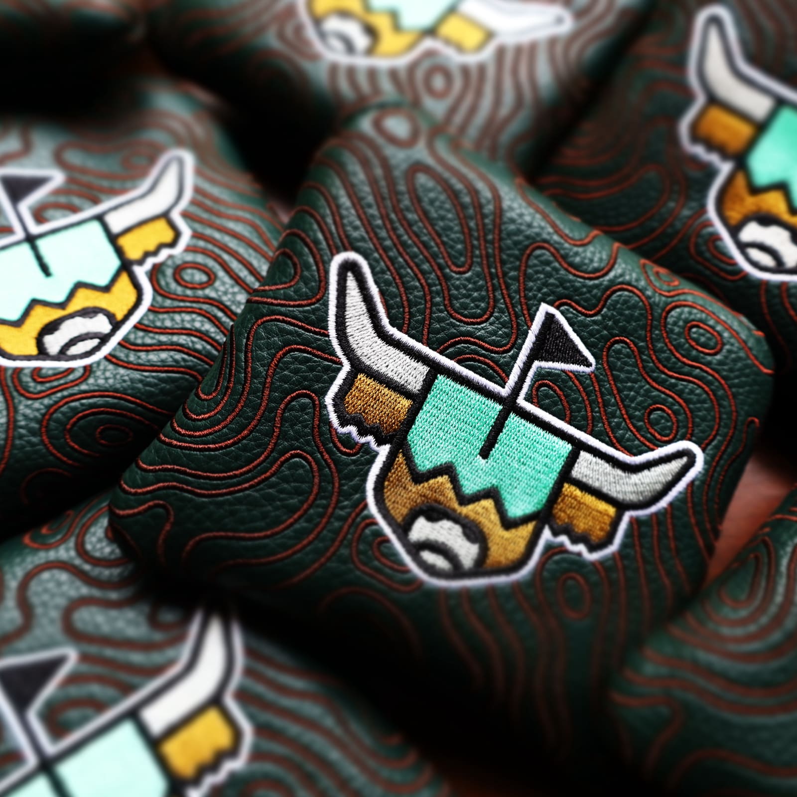 Flat lay of multiple green topography mallet headcovers showcasing Looper logo embroidery