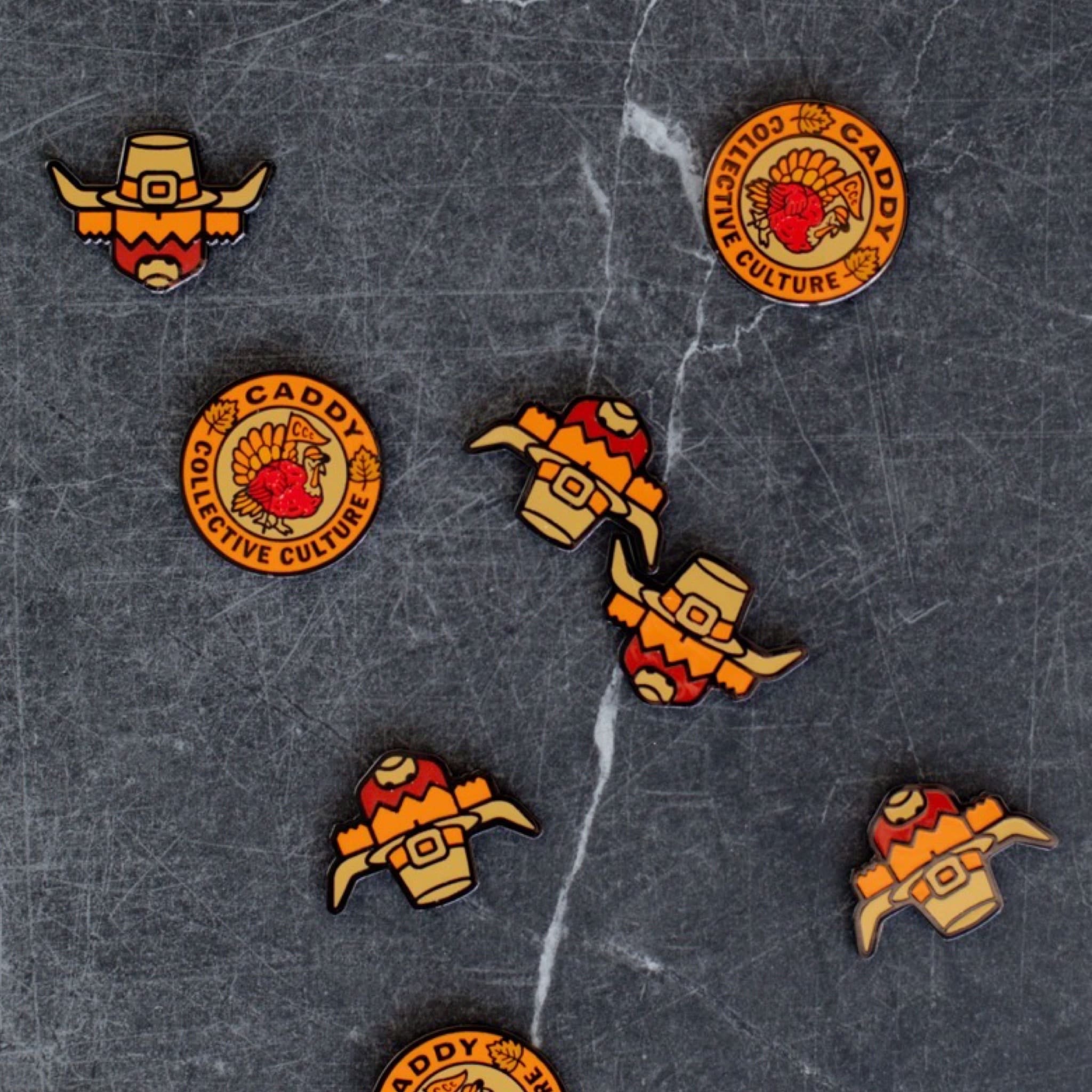 Multiple Harvest Turkey and Pilgrim Looper ball markers by Caddy Collective Culture displayed on a dark stone background.