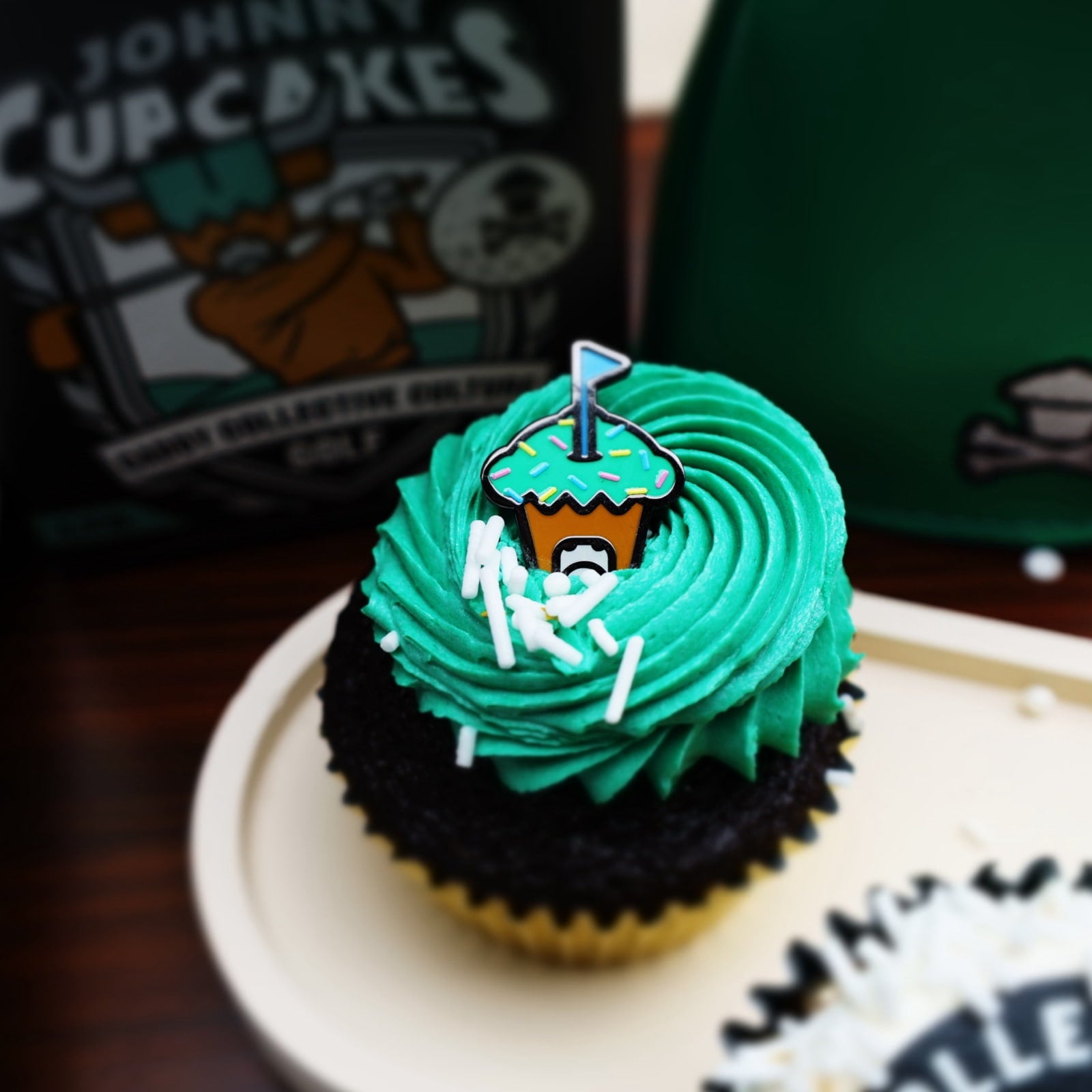 Johnny Cupcakes x Caddy Collective Culture golf ball marker with cupcake and crossbones design styled on green-frosted chocolate cupcake.