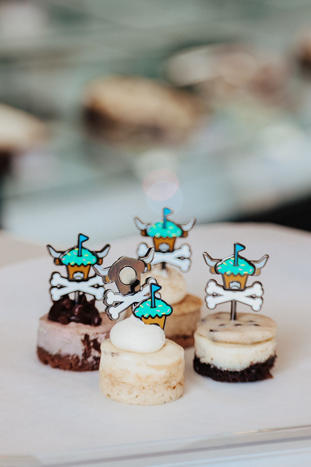 Johnny Cupcakes x Caddy Collective Culture golf ball markers and divot tool displayed on mini cheesecakes with toppings.