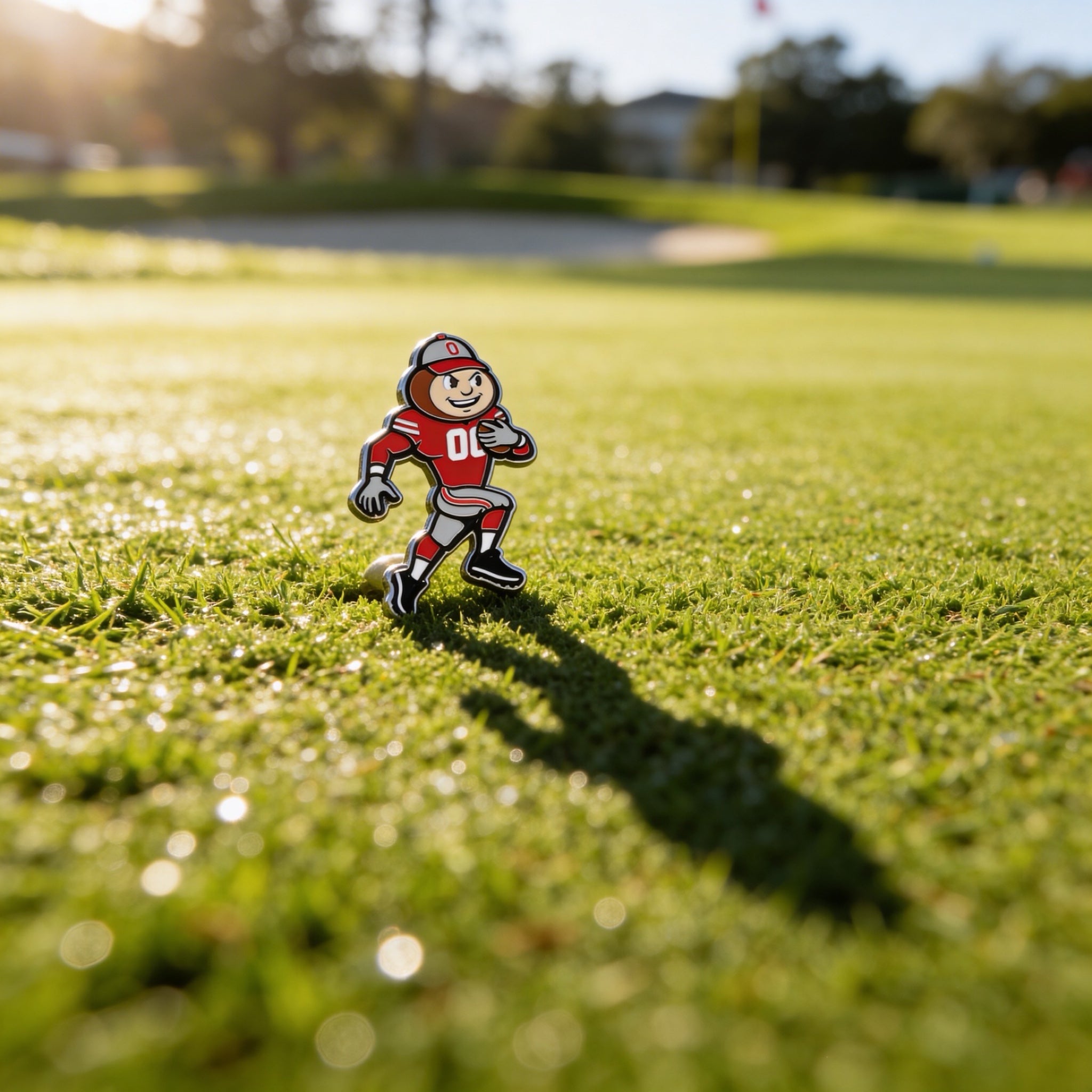 THE Gameday Brutus Ball Marker standing on golf course grass at golden hour with long shadow, Ohio State licensed design by Caddy Collective Culture