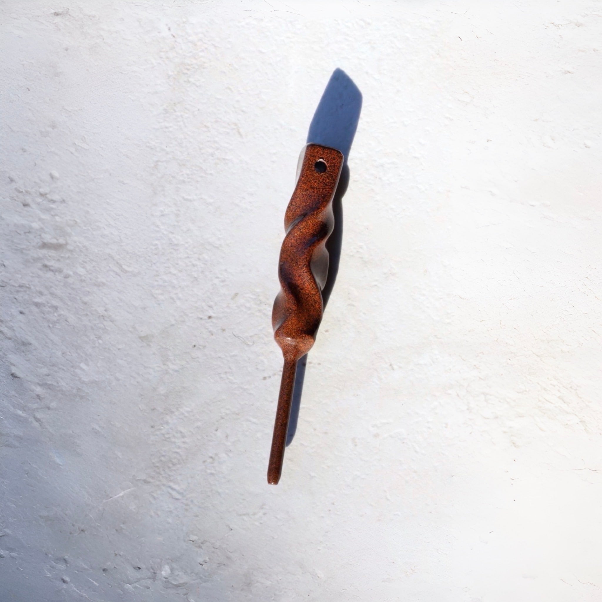 Angled view of the Dual-Twist divot tool in Ithaca bronze from the Twisted Metal collection, casting a natural shadow on a white surface.