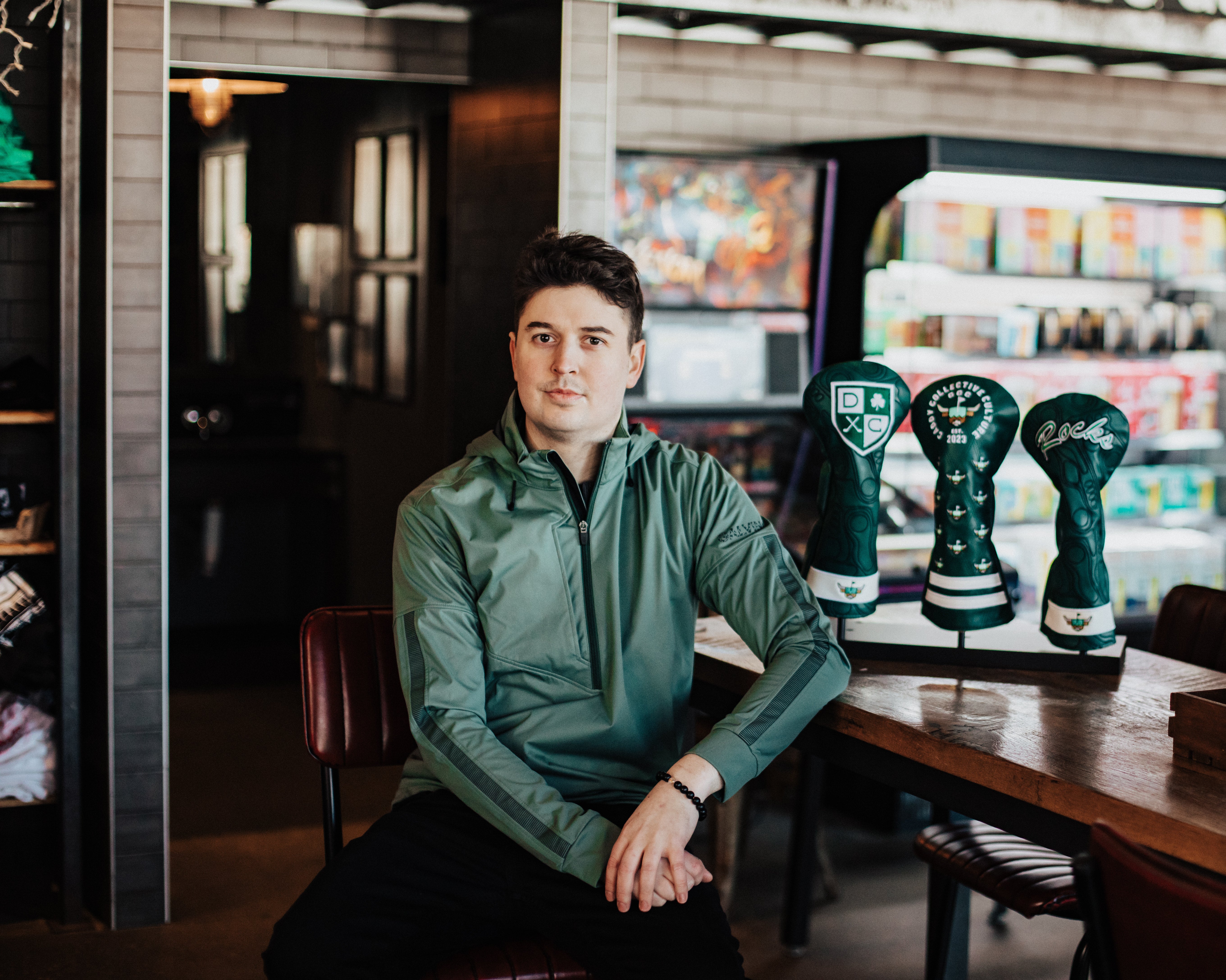 Collin Jenkins, founder of Caddy Collective Culture, sitting beside handcrafted golf headcovers in a boutique setting.