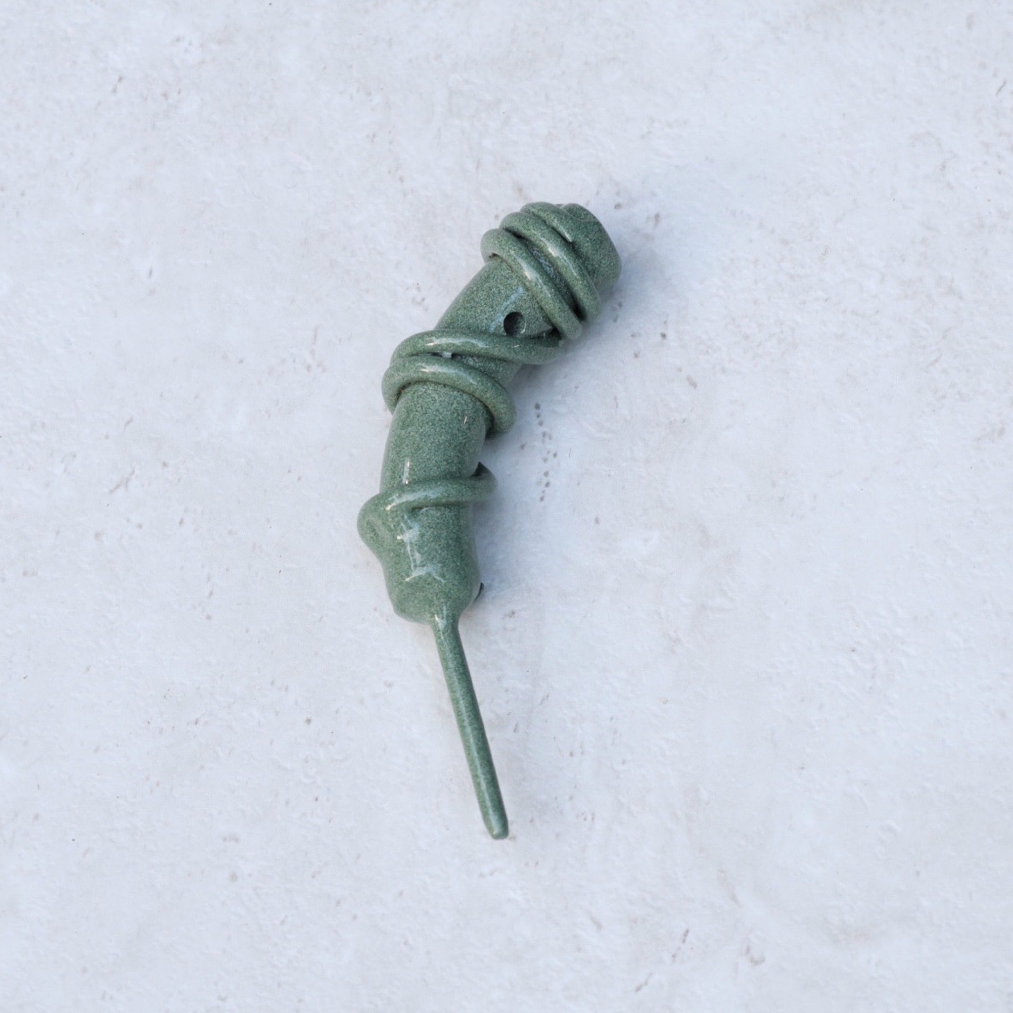 Close-up of the Hand Forged Wrapped Divot Tool in Sage Green finish on a textured stone background, highlighting the sculptural wrapped steel craftsmanship.