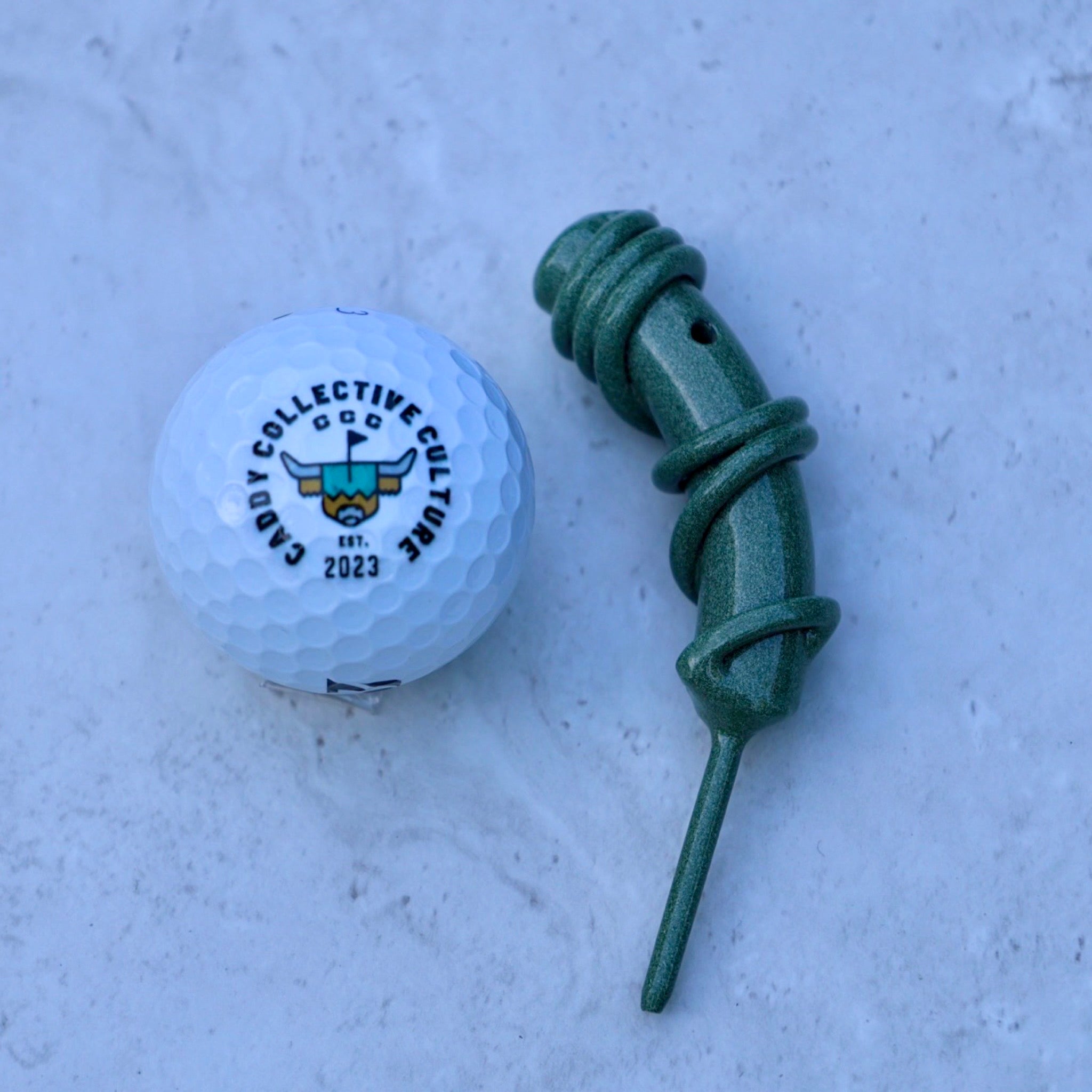 Hand Forged Wrapped Divot Tool in Sage Green finish beside a golf ball by Caddy Collective Culture. Handcrafted single prong golf divot tool for repairing greens.