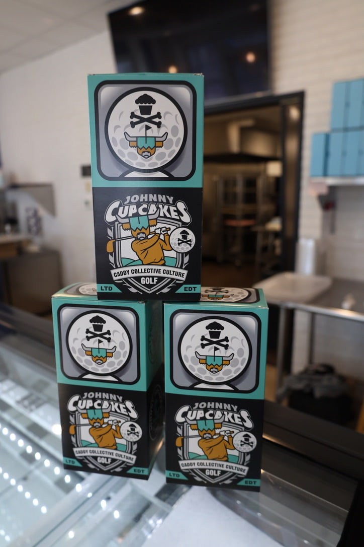 Stack of Johnny Cupcakes x Caddy Collective Culture collectible golf boxes featuring custom artwork with Looper and cupcake skull branding.