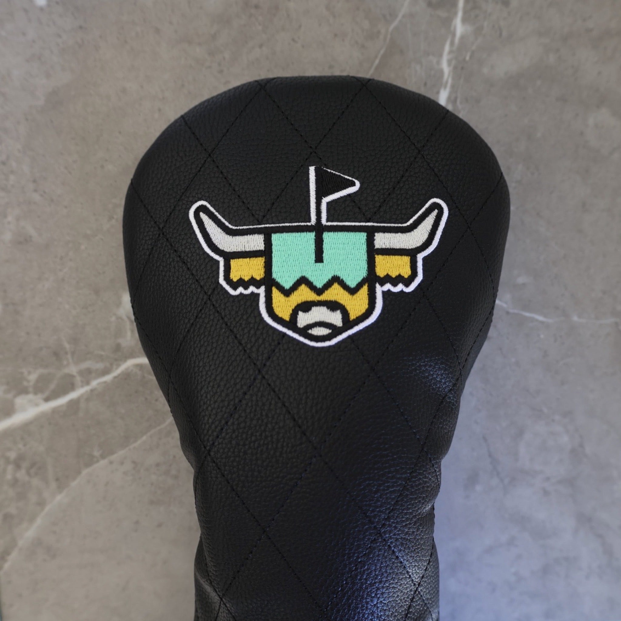 Quilted Heritage Leather Driver Headcover displayed against a stone backdrop, showcasing premium black quilted leather and luxury golf styling.