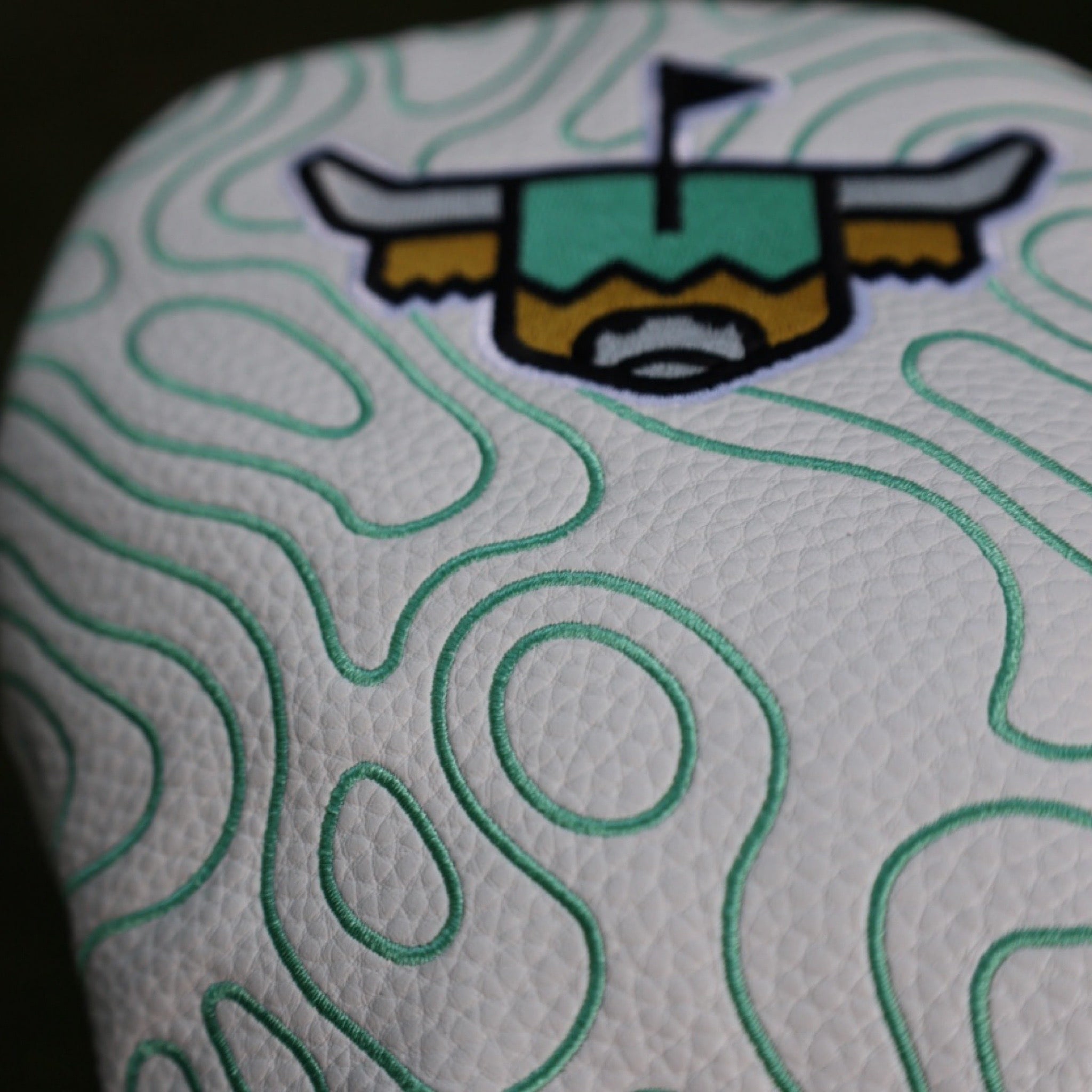 Detailed close-up of the white pebbled grain leather and embroidered green topographic design on the Terrain Driver Headcover.
