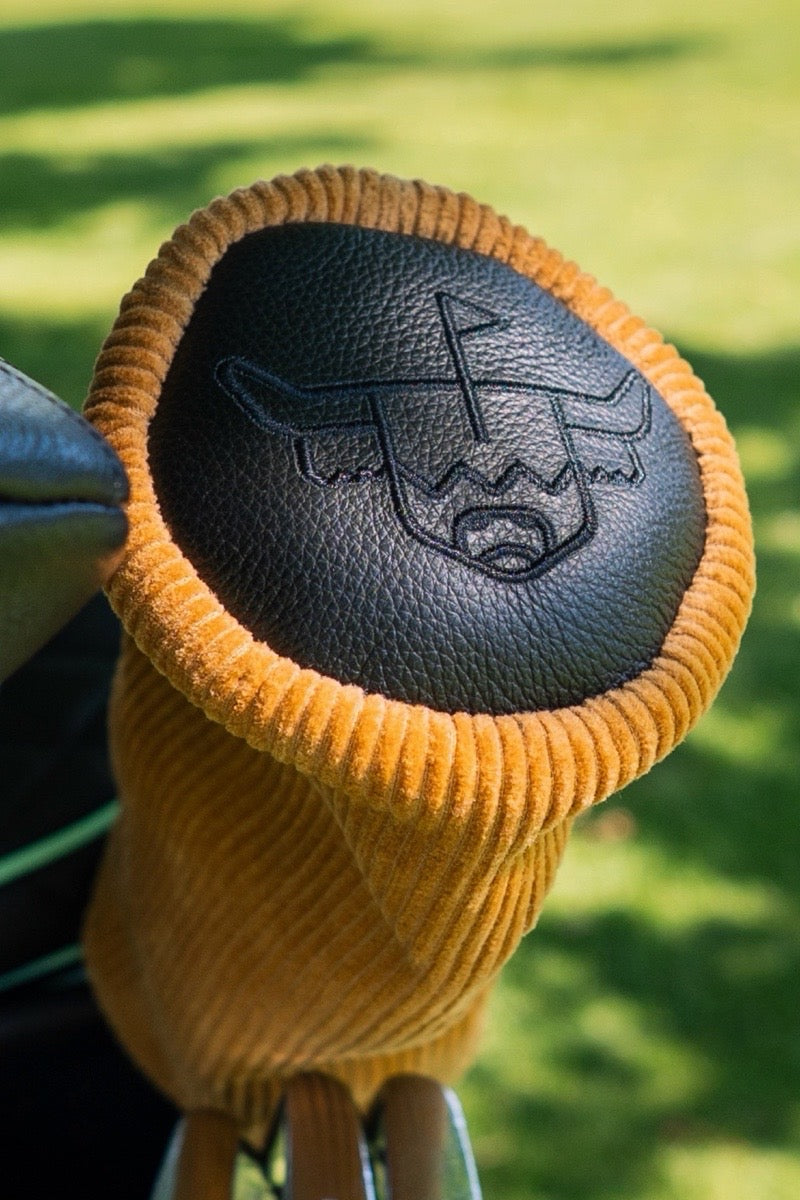 Barrel corduroy golf fairway headcover with black leather top displayed on a golf bag during a sunny round.
