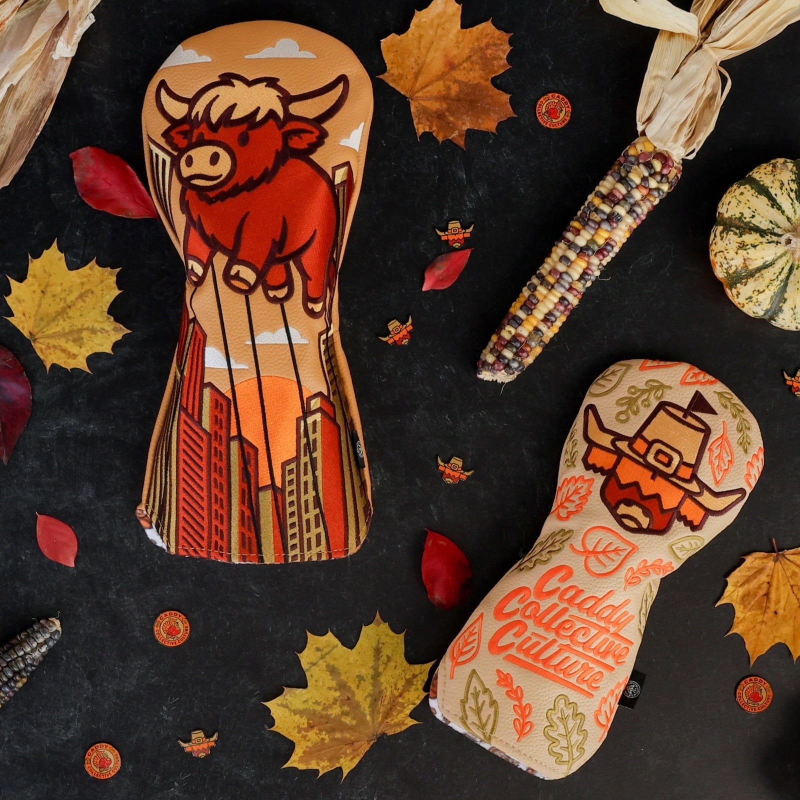 Caddy Collective Culture Thanksgiving golf headcovers displayed with fall leaves, corn, and seasonal harvest props on a dark textured surface.