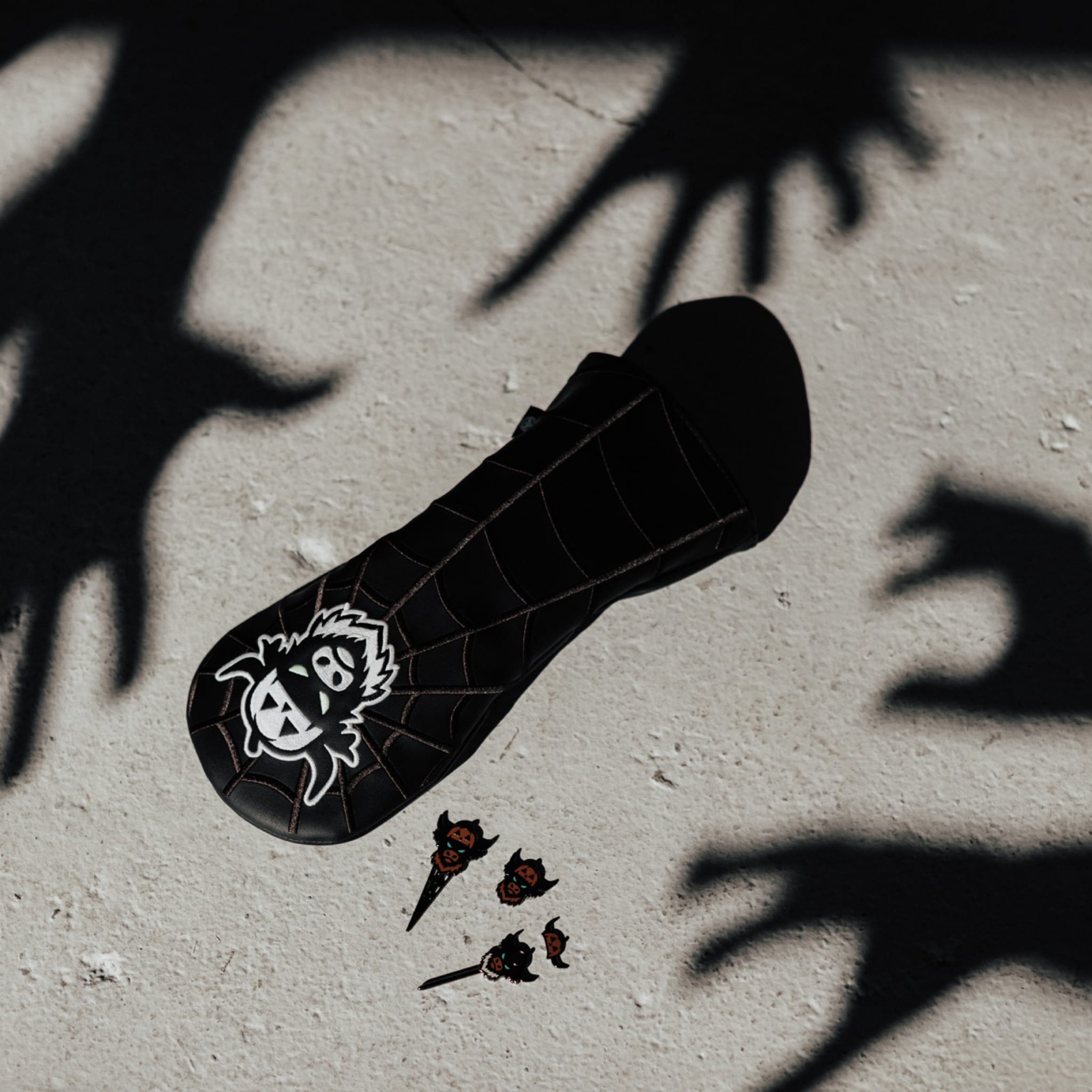 Looper After Dark Halloween golf collection by Caddy Collective Culture featuring a black spiderweb headcover and divot tools surrounded by eerie shadowed hands.