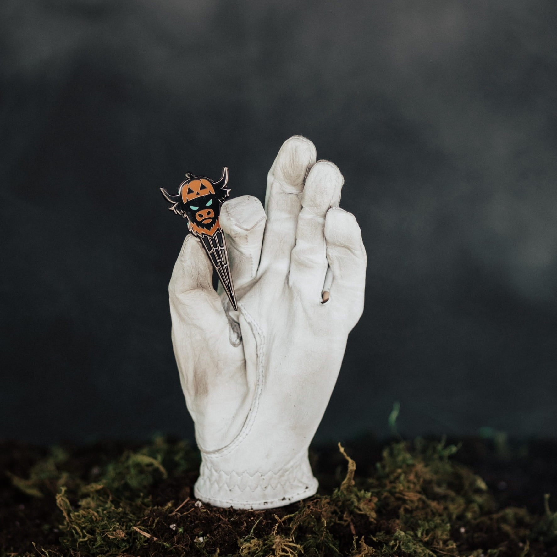 Caddy Collective Culture Looper After Dark Halloween divot tool featuring jack-o’-lantern Looper design displayed in a white golf glove over moss with a dark moody background.