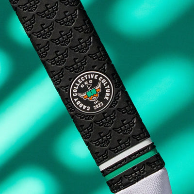 Close-up of a black Garsen putter grip showing the Caddy Collective Culture badge, repeating embossed caddy pattern, green accent ring, and white end cap.
