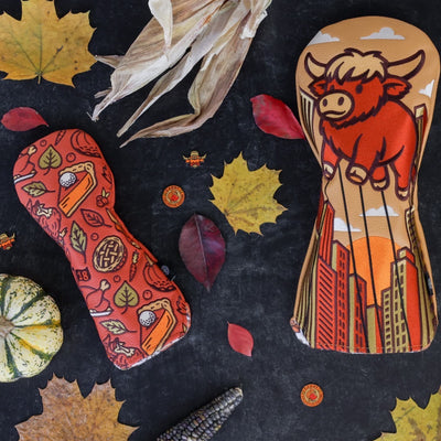 Autumn Feast hybrid headcover shown in a fall-themed flat-lay with leaves, corn, and the Harvest Parade driver headcover.