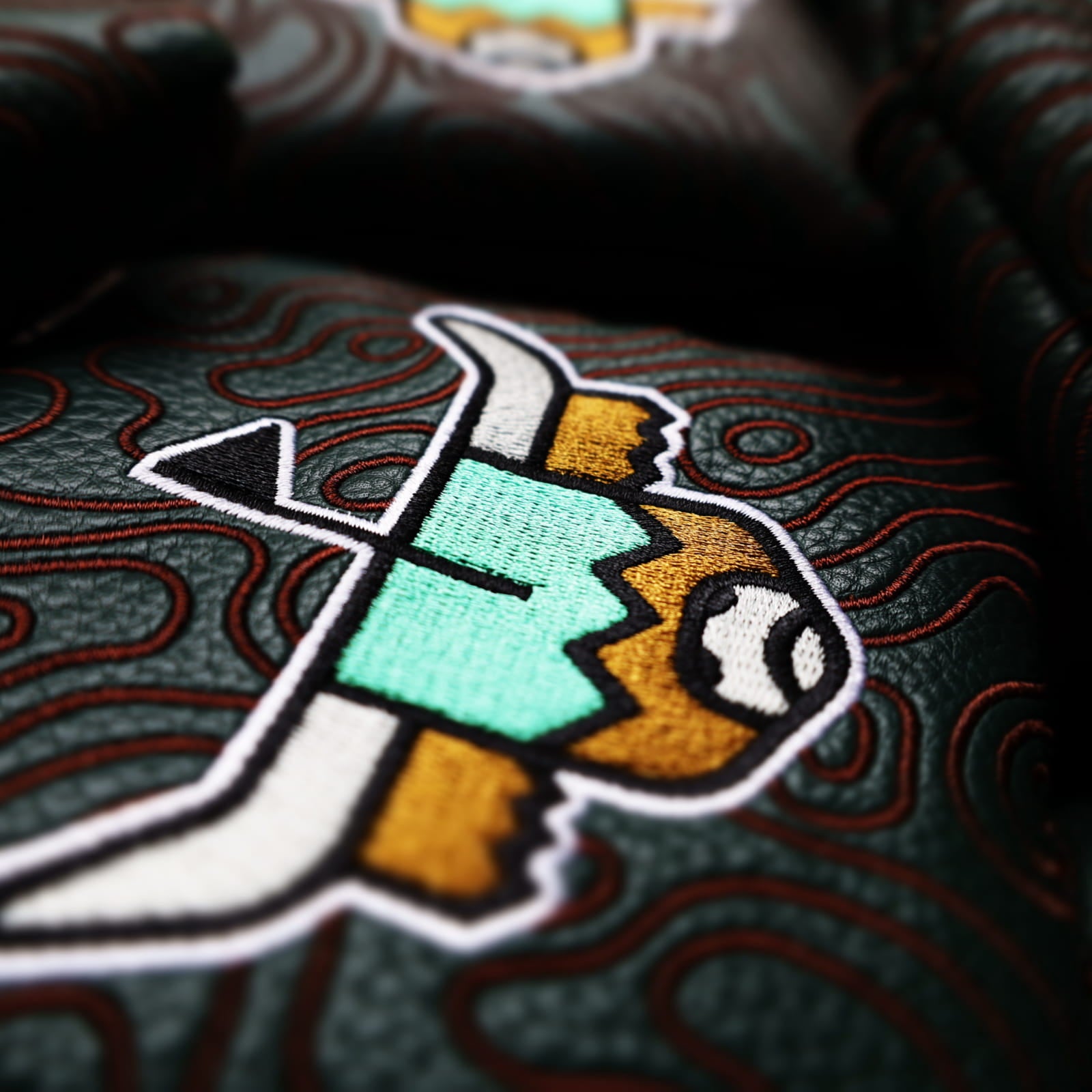 Close-up highlighting embroidery and stitched topography design on green mallet putter headcover
