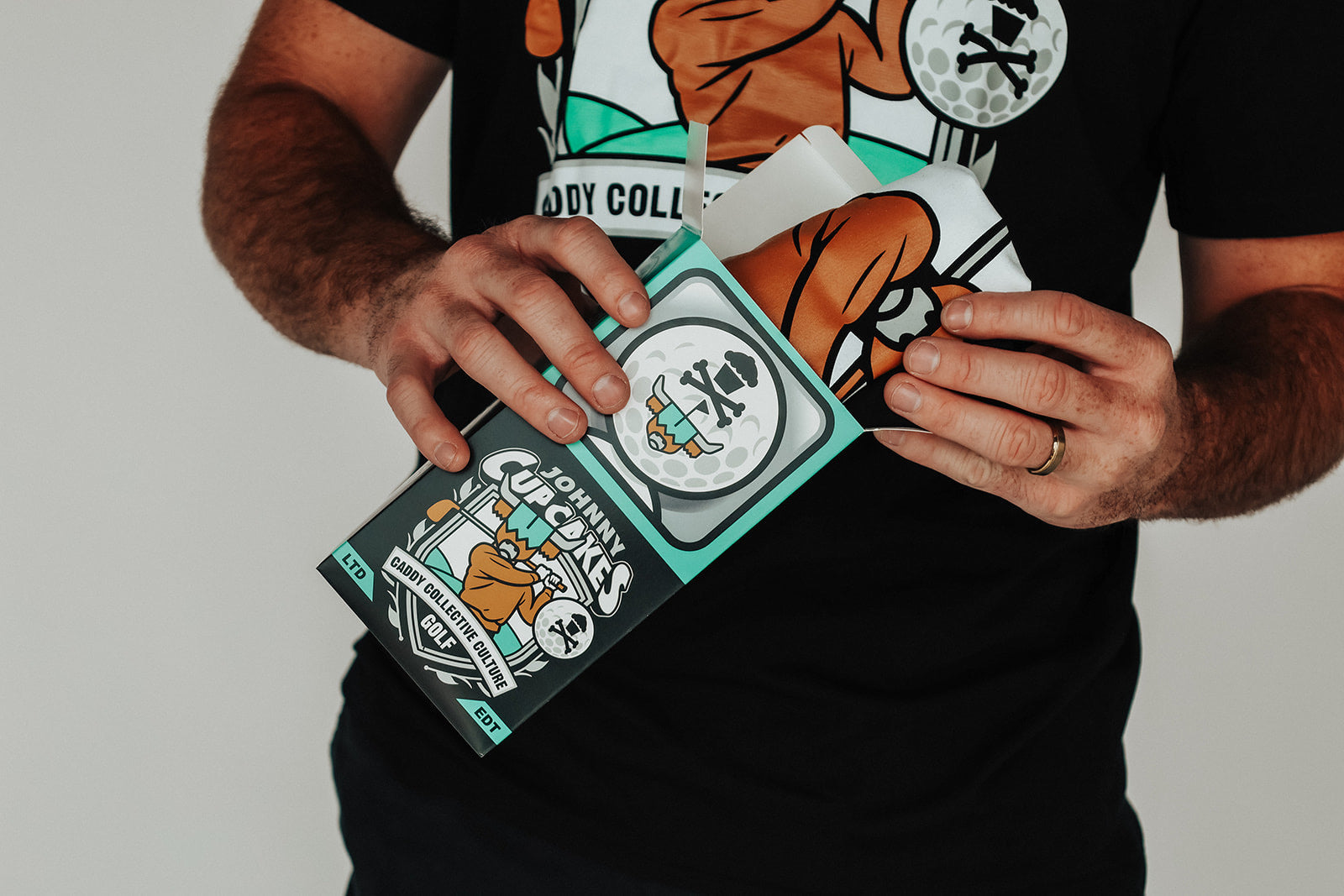 Person unboxing the Johnny Cupcakes x Caddy Collective Culture limited-edition shirt from a custom collector box.