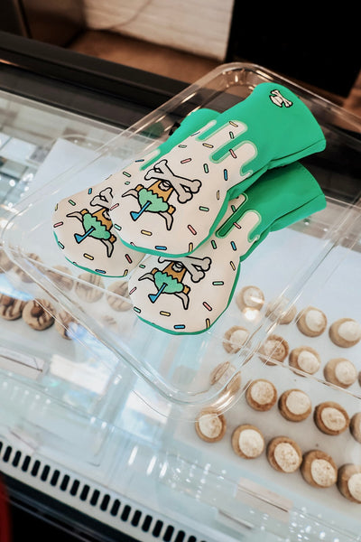 Johnny Cupcakes x Caddy Collective Culture golf hybrid headcovers with sprinkle cupcake design displayed on bakery tray with pastries in background.