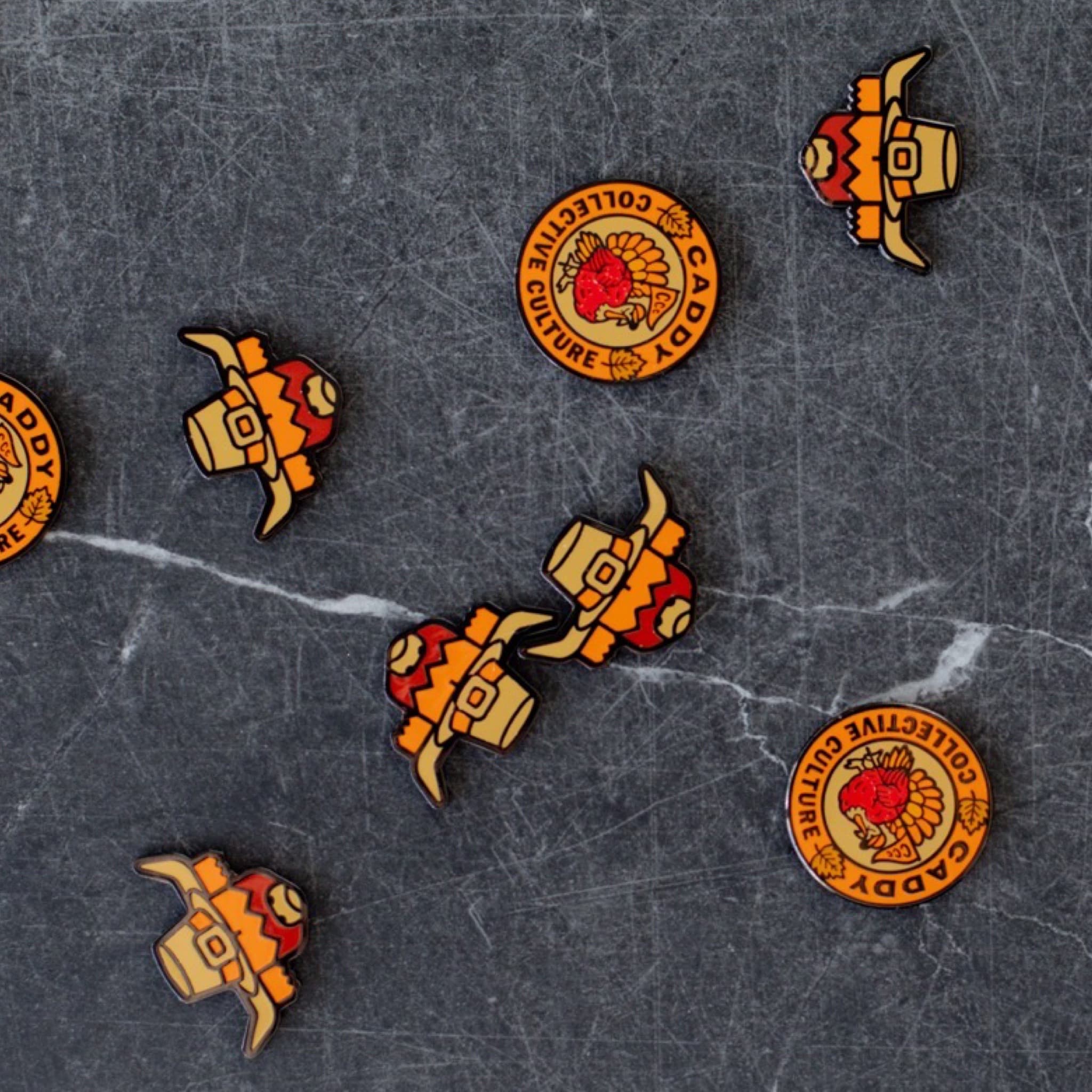Multiple Pilgrim Looper and Harvest Turkey ball markers by Caddy Collective Culture displayed on a dark stone background.