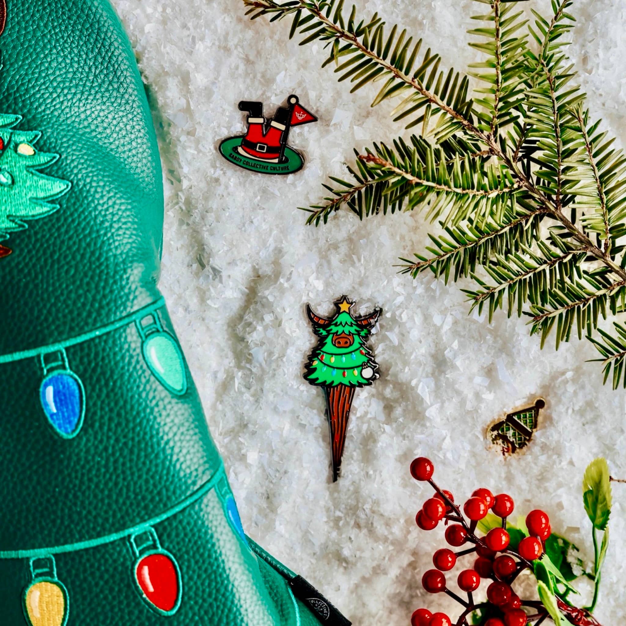 Evergreen Collection golf accessories displayed on snow, featuring the Looper divot tool, ball markers, and festive elements.
