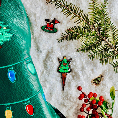 Evergreen Collection golf accessories displayed on snow, featuring the Looper divot tool, ball markers, and festive elements.
