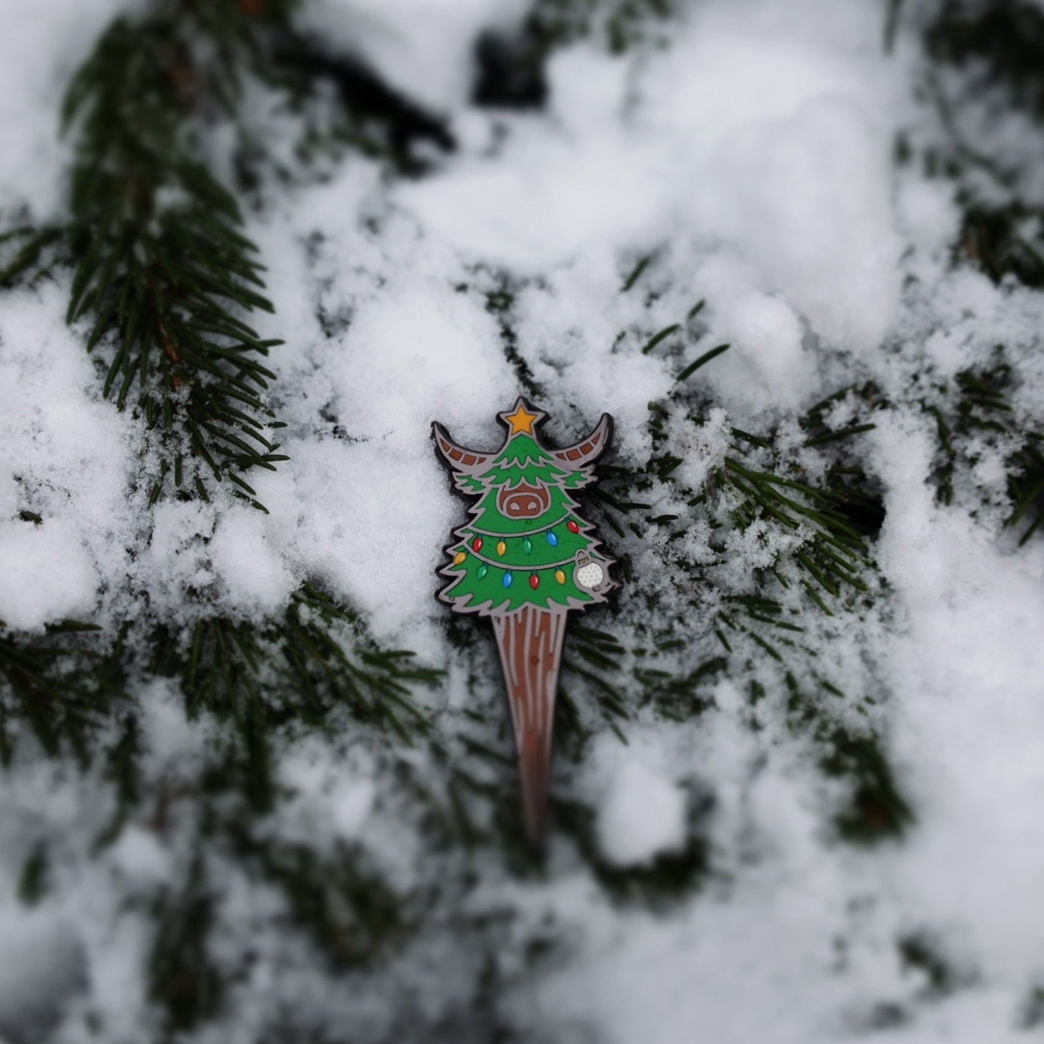 Close-up of the Evergreen Looper divot tool resting in snow with visible enamel details and colors.