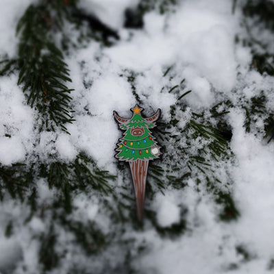 Close-up of the Evergreen Looper divot tool resting in snow with visible enamel details and colors.