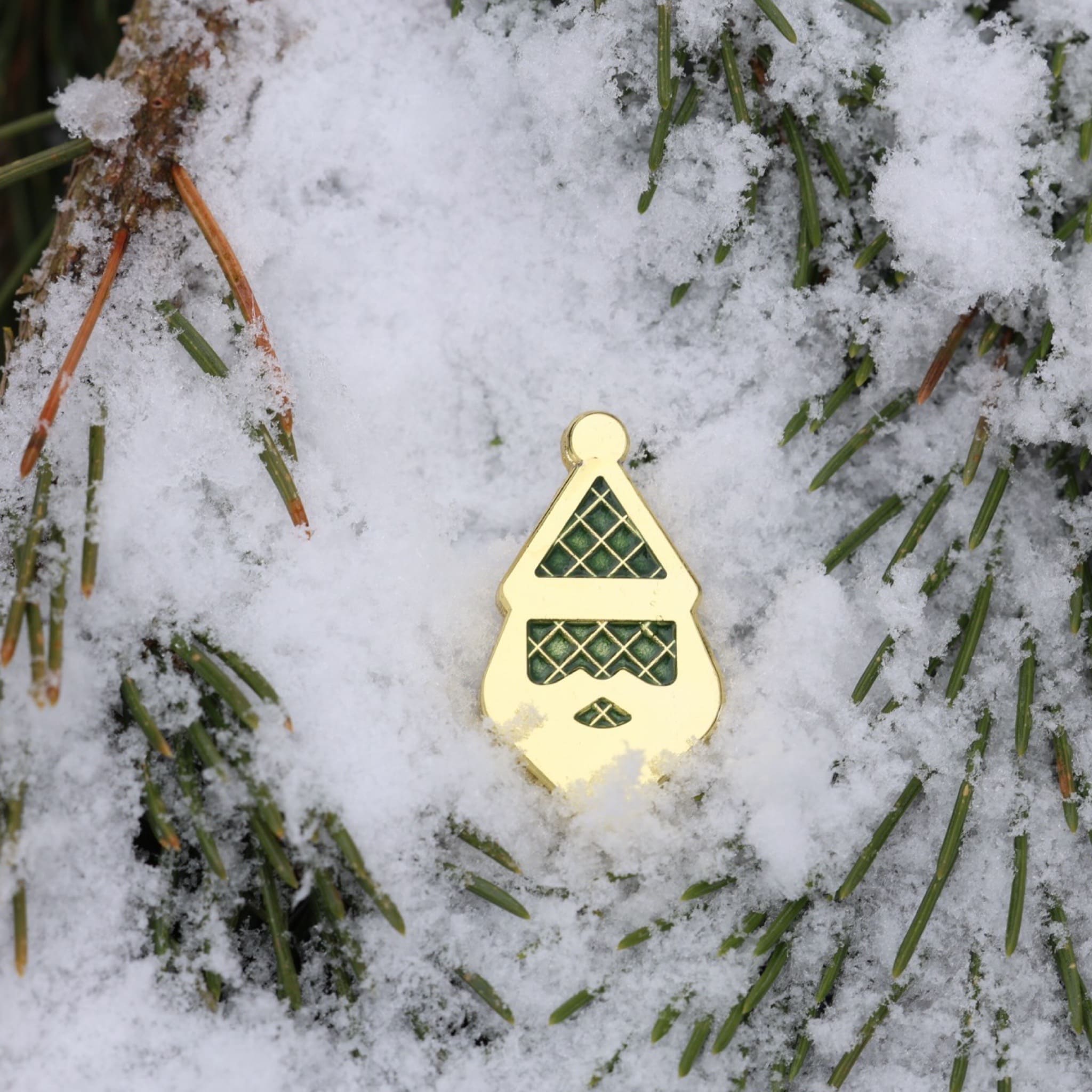 Santa Silhouette golf ball marker partially set in fresh snow among pine branches.