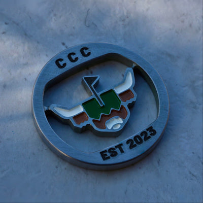 Close-up detail of the First Cut CCC Mark ball marker showing CNC-milled edges, enamel fill, and premium metal finish.