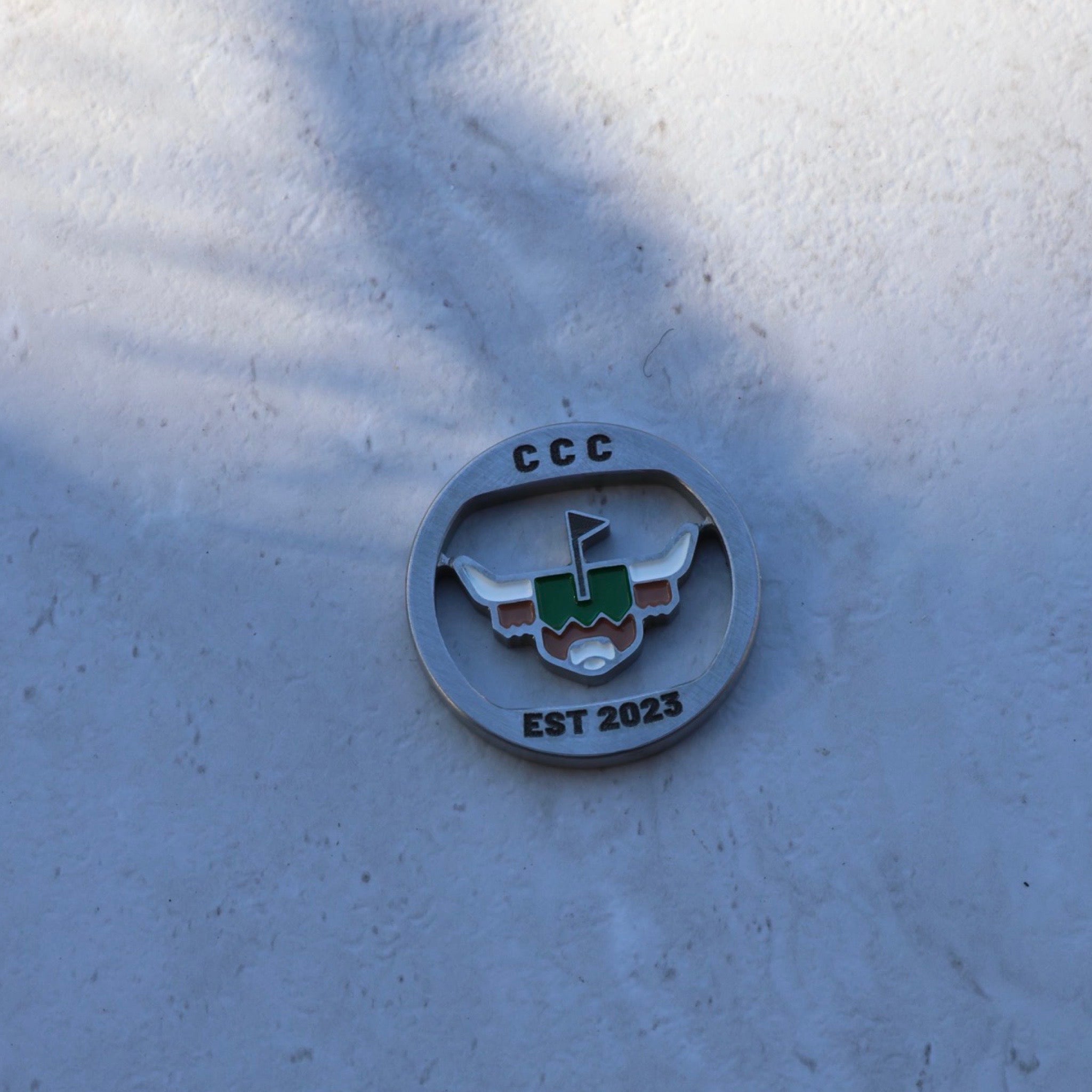 First Cut CCC Mark ball marker photographed in natural light, showing enamel-filled logo and solid metal profile.