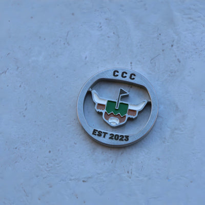 First Cut CCC Mark ball marker centered on stone background, featuring enamel-filled logo and polished metal edge
