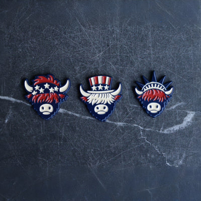 The Founders Collection golf ball markers featuring Patriot, Founder, and Liberty Looper designs displayed on dark marble background