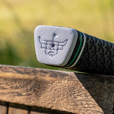 White textured end cap on a Garsen putter grip featuring an embossed golf bull logo, with the black patterned grip extending into the background.