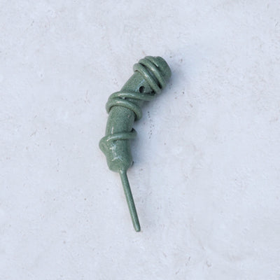 Close-up of the Hand Forged Wrapped Divot Tool in Sage Green finish on a textured stone background, highlighting the sculptural wrapped steel craftsmanship.