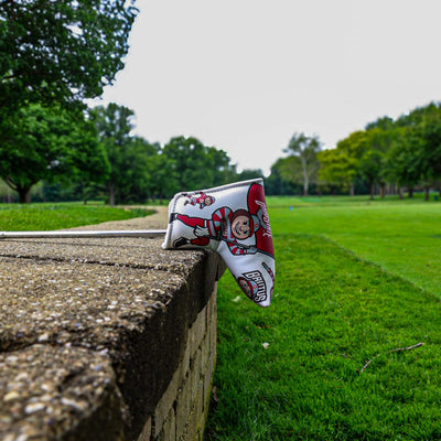 Ohio State Brutus blade putter cover displayed on a stone wall overlooking a golf course fairway.