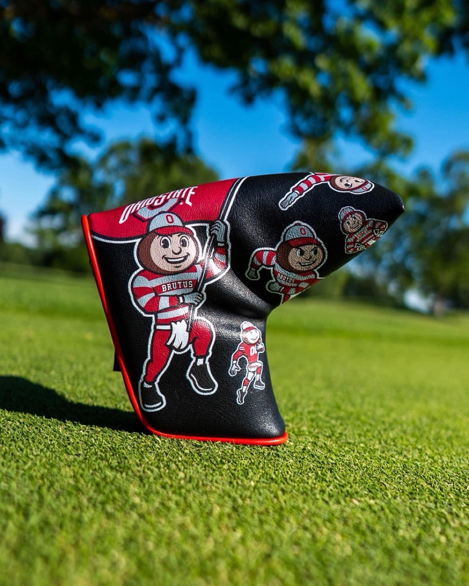Black Ohio State Brutus Montage blade putter cover featuring vintage Brutus Buckeye artwork displayed on a putting green.