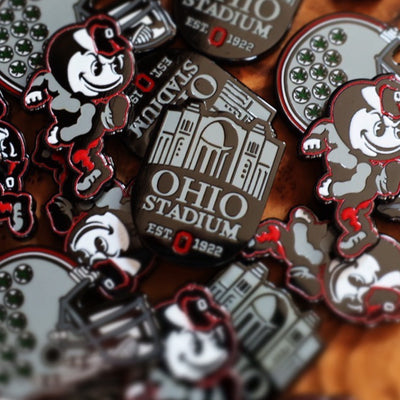 Ohio State THE Horseshoe Ball Marker displayed among Buckeye Right Helmet and Heritage Brutus markers on wood surface