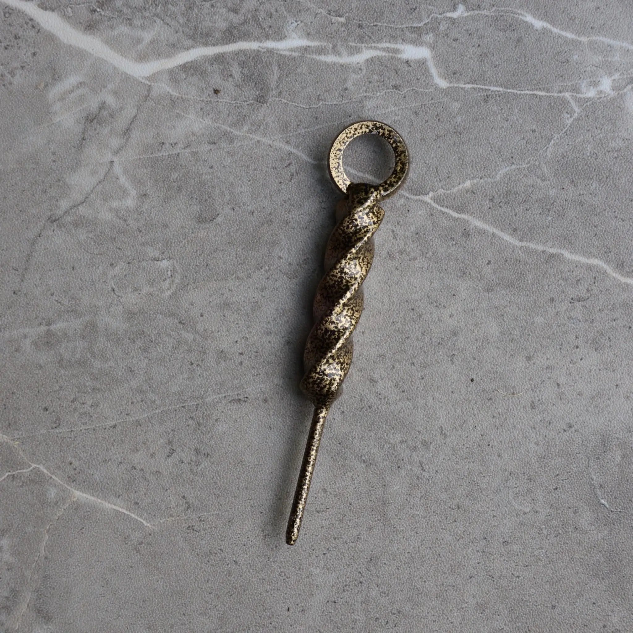 Front view of the Twisted Coil Golf Divot Tool featuring a hand-forged spiral steel body with an antique gold finish on a stone surface.