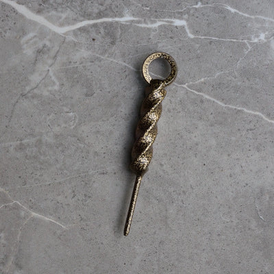 Front view of the Twisted Coil Golf Divot Tool featuring a hand-forged spiral steel body with an antique gold finish on a stone surface.
