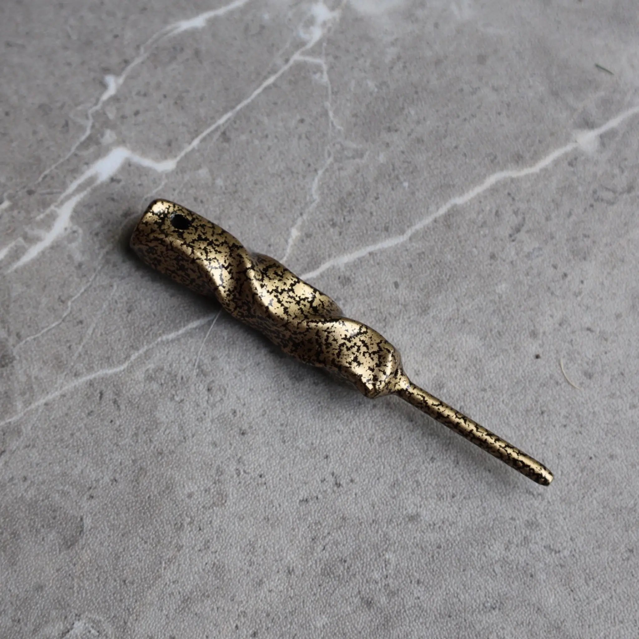 Twisted Column Golf Divot Tool handcrafted from forged steel with an antique gold finish shown at an angled view on a stone surface.