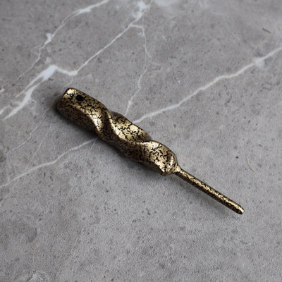 Twisted Column Golf Divot Tool handcrafted from forged steel with an antique gold finish shown at an angled view on a stone surface.